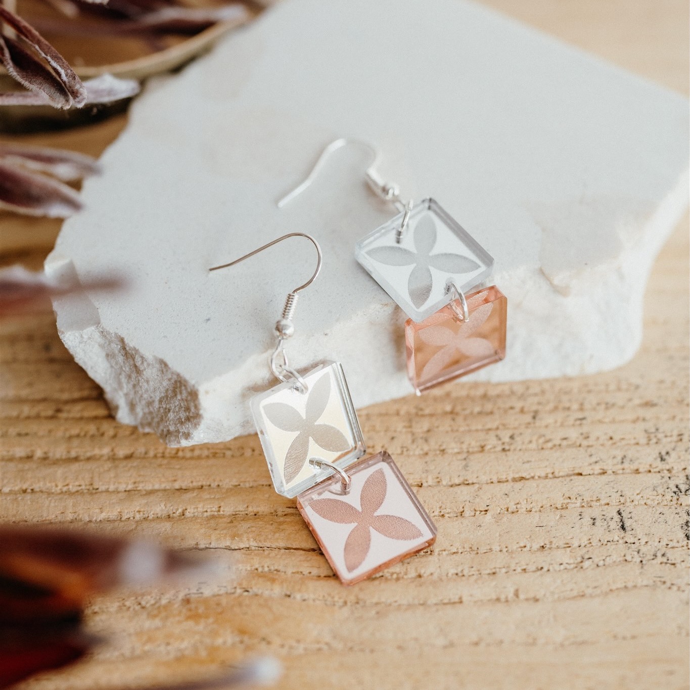 Pasifika Signature earrings styled on natural stone — peach and mirror acrylic squares with floral patterns